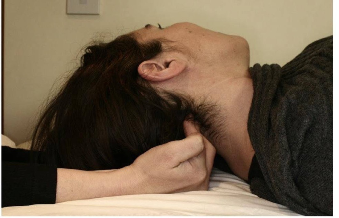 A person lying on their side with their head turned, a practitioner's hand supporting the back of the neck.