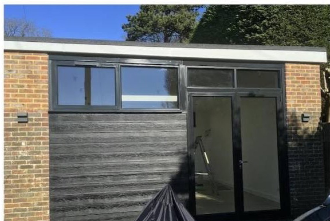 The outside of the converted garage: brick either side, grey timber cladding, a long window and glazed double doors.